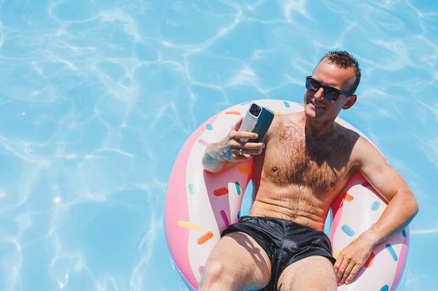 An attractive man is relaxing on an inflatable ring in the pool A man in the pool is talking on the phone vacation and free time concept