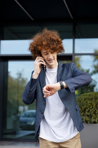 Attractive man looking at clock talking on phone near modern office Successful businessman outdoors