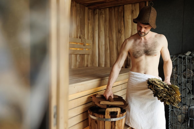 Attractive man with a bath broom in a sauna