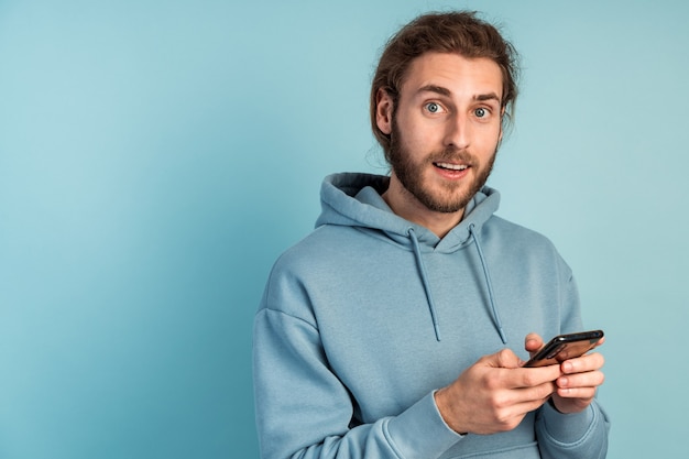 Attractive man with a beard is holding a smartphone, he is surprised by something.