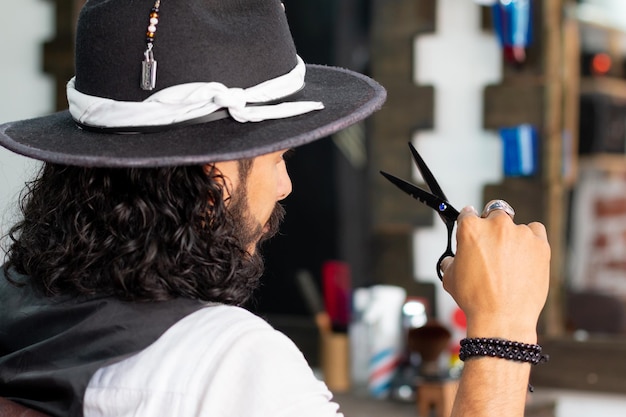 Attractive man with black scissors in his hands looking in the mirror Latino barber