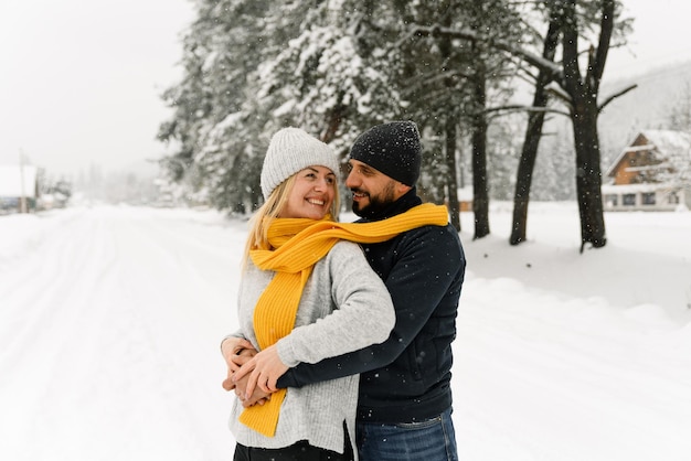 Attractive man and woman cuddling in the frosty forest. Adult couple in sweaters have fun on walk. Romantic date in winter time.Winter lovestory