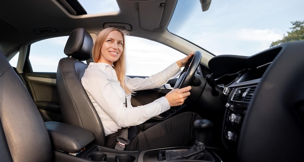 Attractive mature woman in formal clothes fastening with seatbelt while driving modern car Caucasian business lady with blond hair enjoying her way to work