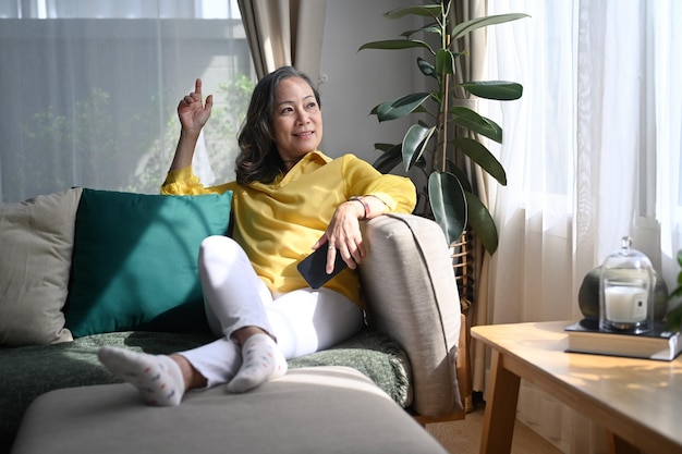 Attractive mature woman resting on comfortable sofa and looking through the window