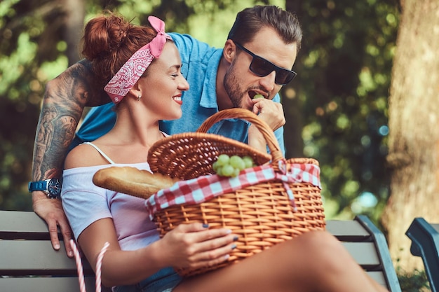 Attractive middle age couple during dating, enjoying a picnic on a bench in the city park.