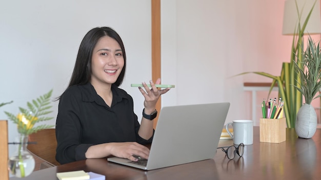 Attractive millennial woman talking on cellphone and using laptop computer at home office