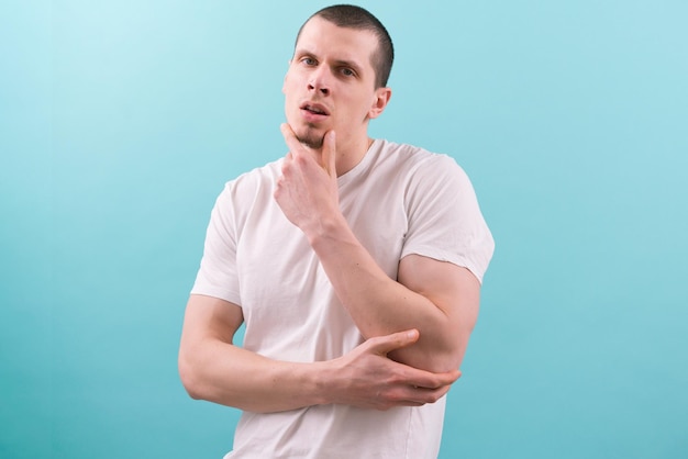 An attractive model man in a white tshirt holds his face with an open mouth on a blue background Attractive Muscular Masculine Macho Manly Brave Potent Virile Pose Perfect Confident