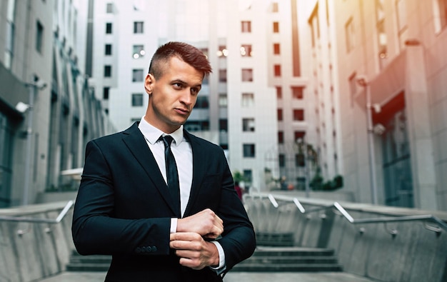 Attractive modern businessman in a black suit stands with a serious look in front of him against the backdrop of the city