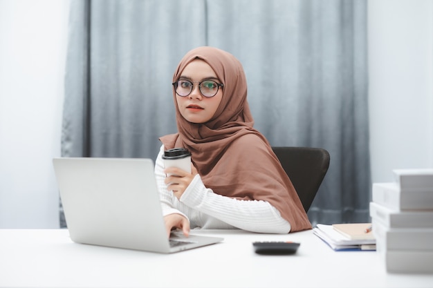 Attractive muslim business woman hand holding a cup of coffee while working in home office.