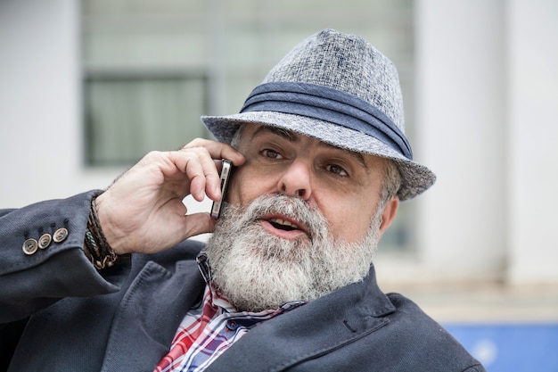 Attractive old man with beard and hat talking on phone