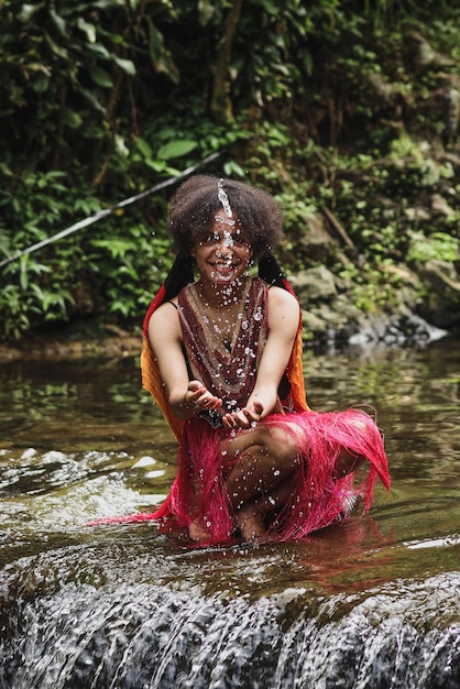 Attractive papua young girl of dani tribe in traditional clothes splashing water over smiling face