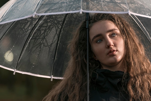 Attractive pensive young woman with lush brown hair under transparent umbrella Autumn portrait Sad image