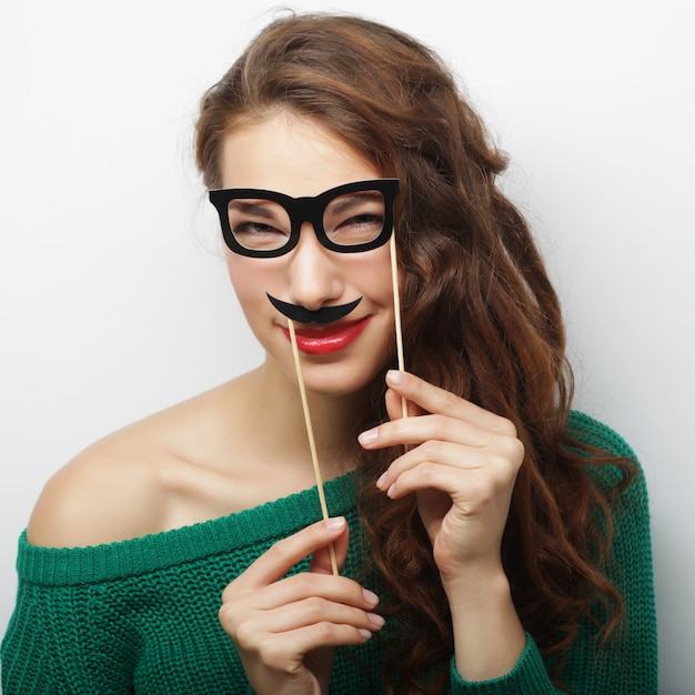 Attractive playful young woman holding mustache and glasses 