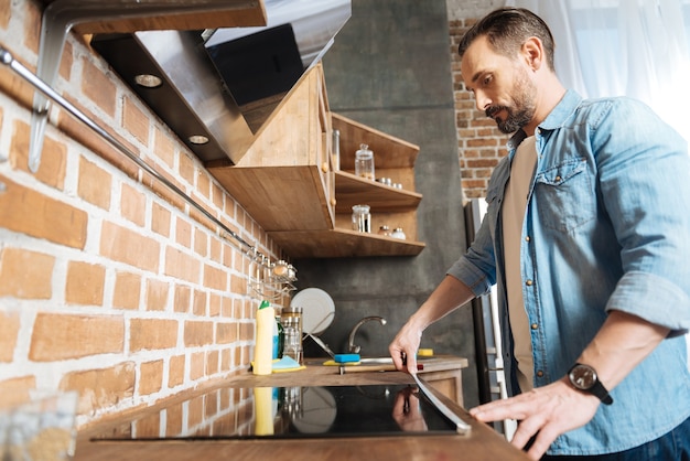 Attractive pleasant bearded man posing in profile while staring down and measuring surface