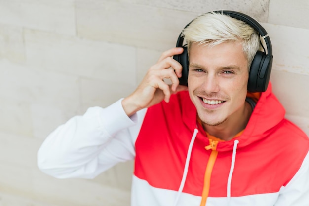 Attractive portrait of happy male dressed in red sportswear resting after physical activities in open air in park Young handsome man smiling and listening to music with headphones outdoor