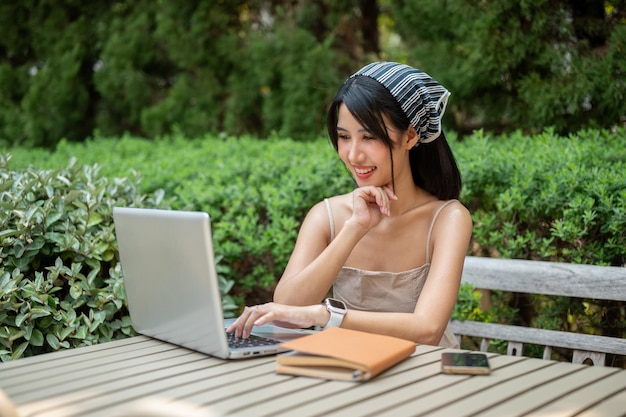 An attractive positive Asian woman working on her laptop computer at a table in a green garden