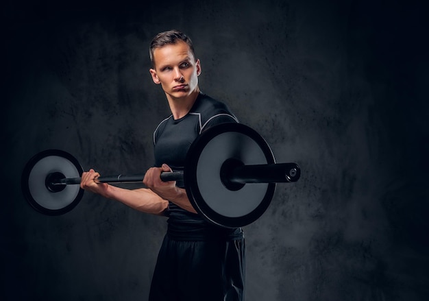 Attractive power lifter holds barbell over dark grey background.