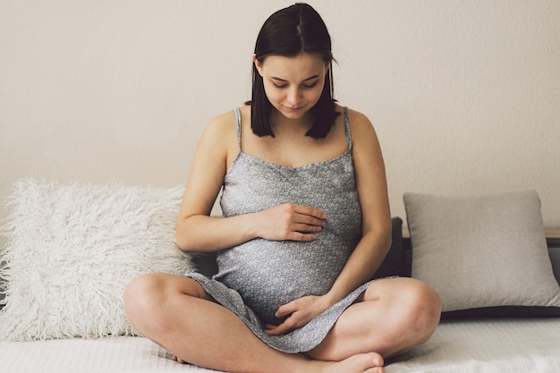 Attractive pregnant woman is sitting in bed and holding her belly