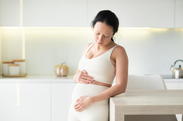 An attractive pregnant woman is standing in the kitchen of her home