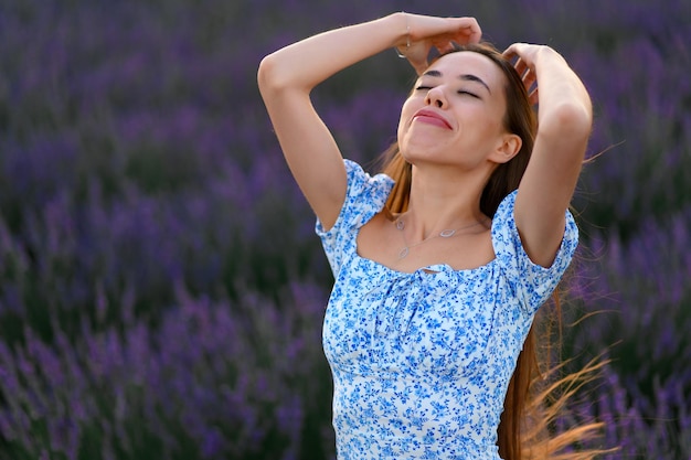 Attractive slender happy girl in a blue dress in a lavender field at sunset