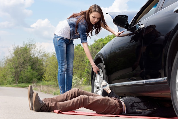 Attractive slender young female driver assisting a mechanic working on her car