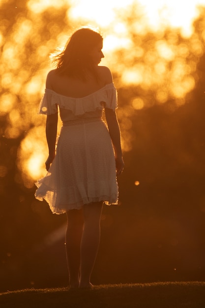 Attractive slender young woman in a white dress dancing on the background of an orange sunset