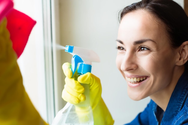 Attractive smiling Woman Washing the Window with spray and rag