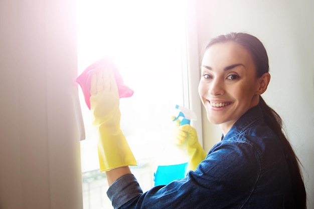 Attractive smiling Woman Washing the Window with spray and rag