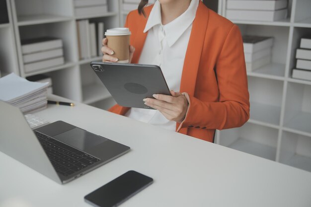 Attractive smiling young asian business woman work at home office Asian woman working on laptop computer holding tablet