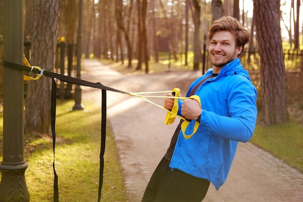 Attractive sporty male exercising with fitness trx strips in a park.