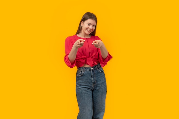 Attractive student girl in youth clothes looks into camera and points fingers at you Portrait on yellow background Mock up copy space