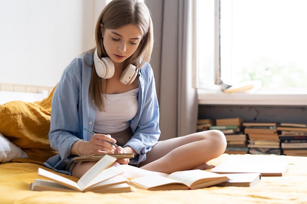 Attractive student woman laying on her bed at home while writing and working on her homework from college preparing for exams