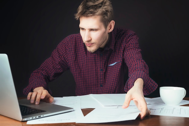 Attractive student work with paper and laptop and drink coffe on dark background b