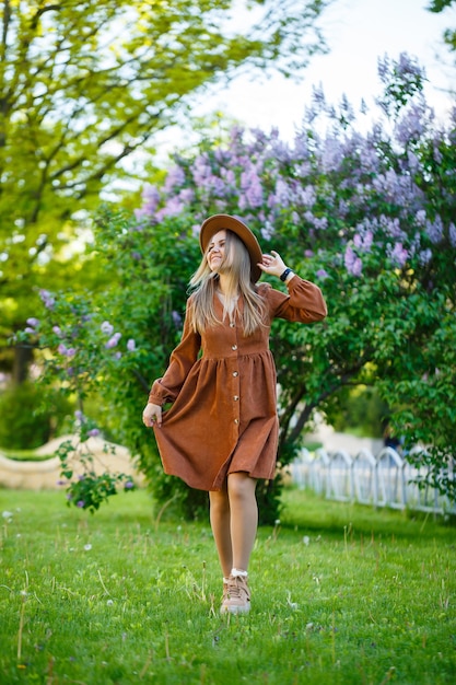 Attractive stylish smiling girl with long hair walks in the park, wearing a warm brown dress with a hat. Young woman of European appearance