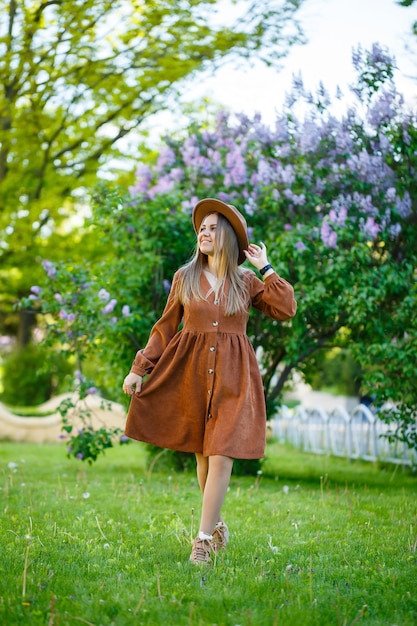 Attractive stylish smiling girl with long hair walks in the park, wearing a warm brown dress with a hat. Young woman of European appearance