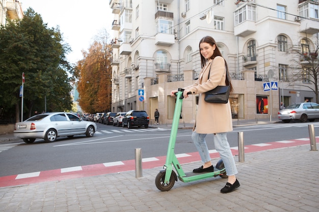 Attractive stylish woman riding electric scooter on the sidewalk in the city, copy space