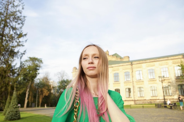 Attractive stylish woman with pink hair smiling enjoying warm autumn weather in city park