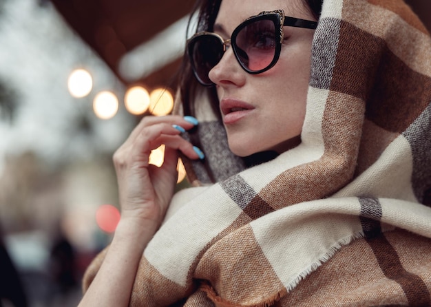 Attractive stylish young brunette female face in sunglasses covered with motley scarf