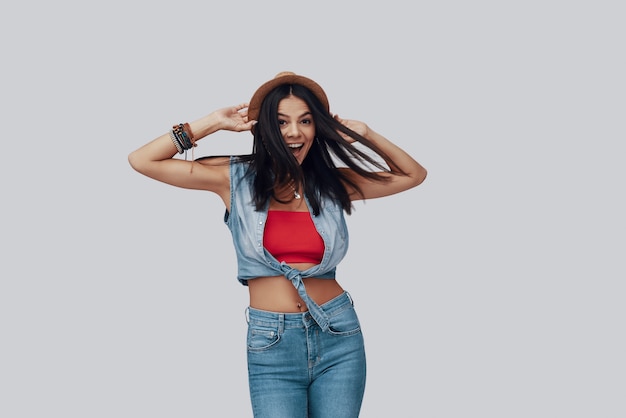 Attractive stylish young woman looking at camera and smiling while standing against grey background