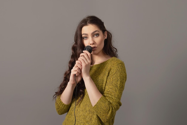 Attractive teenager woman speaking with a microphone against gray background conference speaker