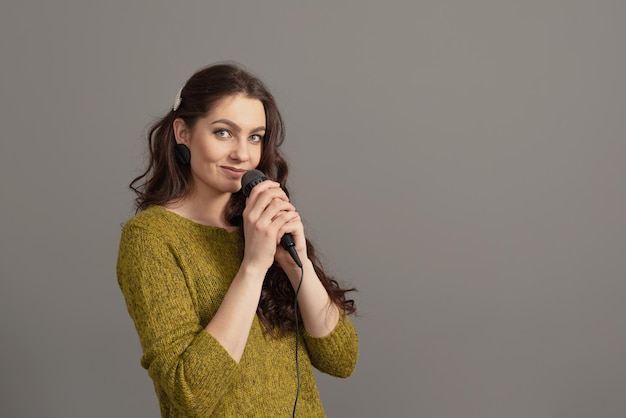 Attractive teenager woman speaking with a microphone against gray background conference speaker