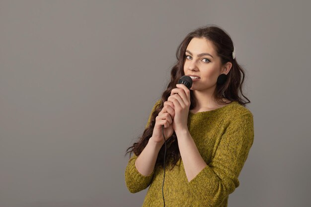 Attractive teenager woman speaking with a microphone against gray background conference speaker