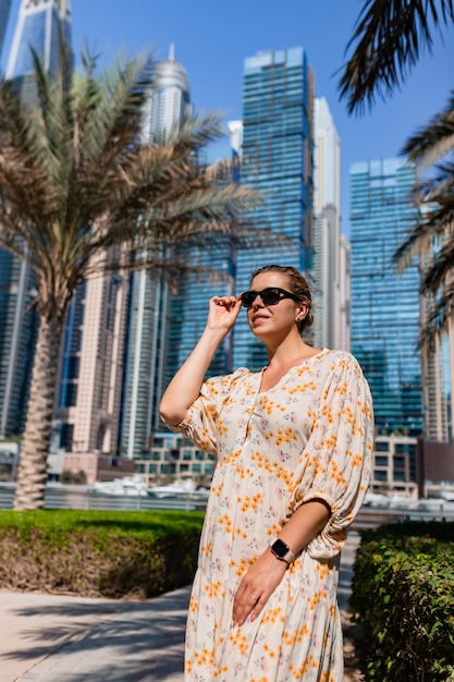 Attractive traveler woman wearing a long dress walking on a promenade in Dubai Marina district Travel destinations and tourist lifestyle in UAE