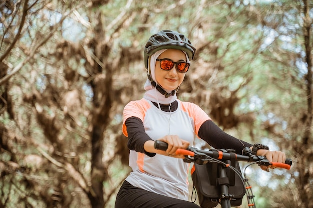 Attractive veiled girl in sunglasses smiling while riding bicycle