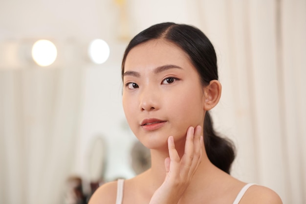 Attractive Vietnamese woman looking at her face in the mirror