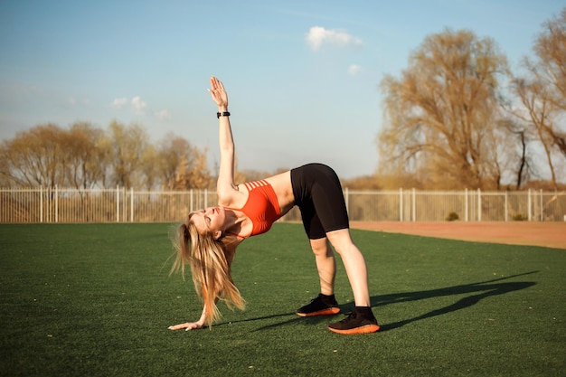 Attractive woman exercising outdoors at the stadium in spring bending over and stretching her arm