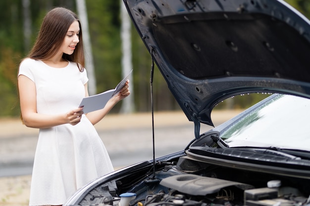 Attractive woman in front of her car broken car with user guide