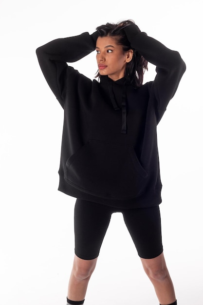 Attractive woman of Latin appearance wears a dark hoodie on a white isolated background The girl looks sexy and happy The elegant brunette is wearing a black sweatshirt Allseason clothing