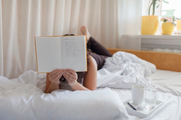 Attractive woman lying in bed practicing stress relief challenge with journal about feeling