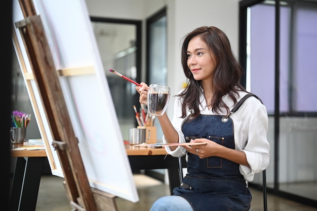 Attractive woman painter drinking coffee and painting picture on canvas